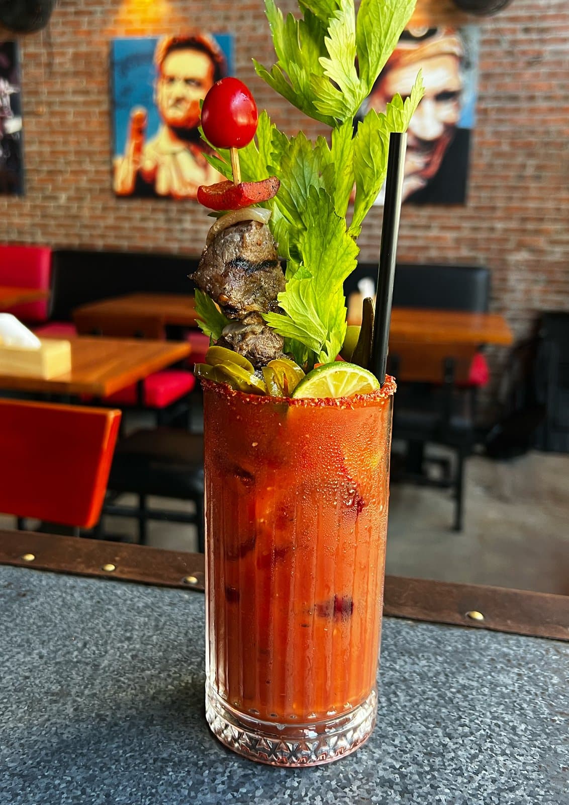 Ly Bloody Bull trên quầy bar, phía sau là tường gạch và ghế đỏ.