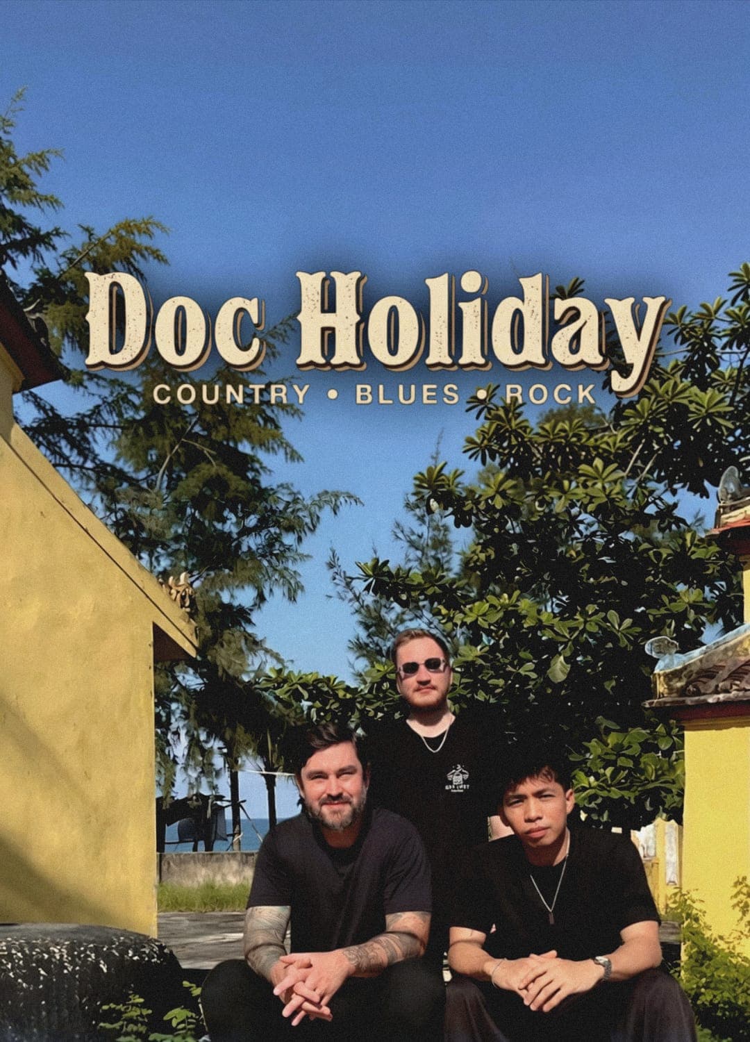 Doc Holiday, country, blues and rock: three men from the band in black T-shirts, outside under the trees.